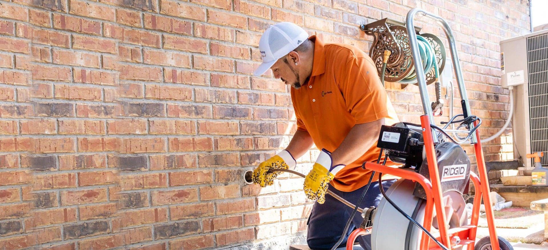 Plumber using a drain snake on a brick wall.