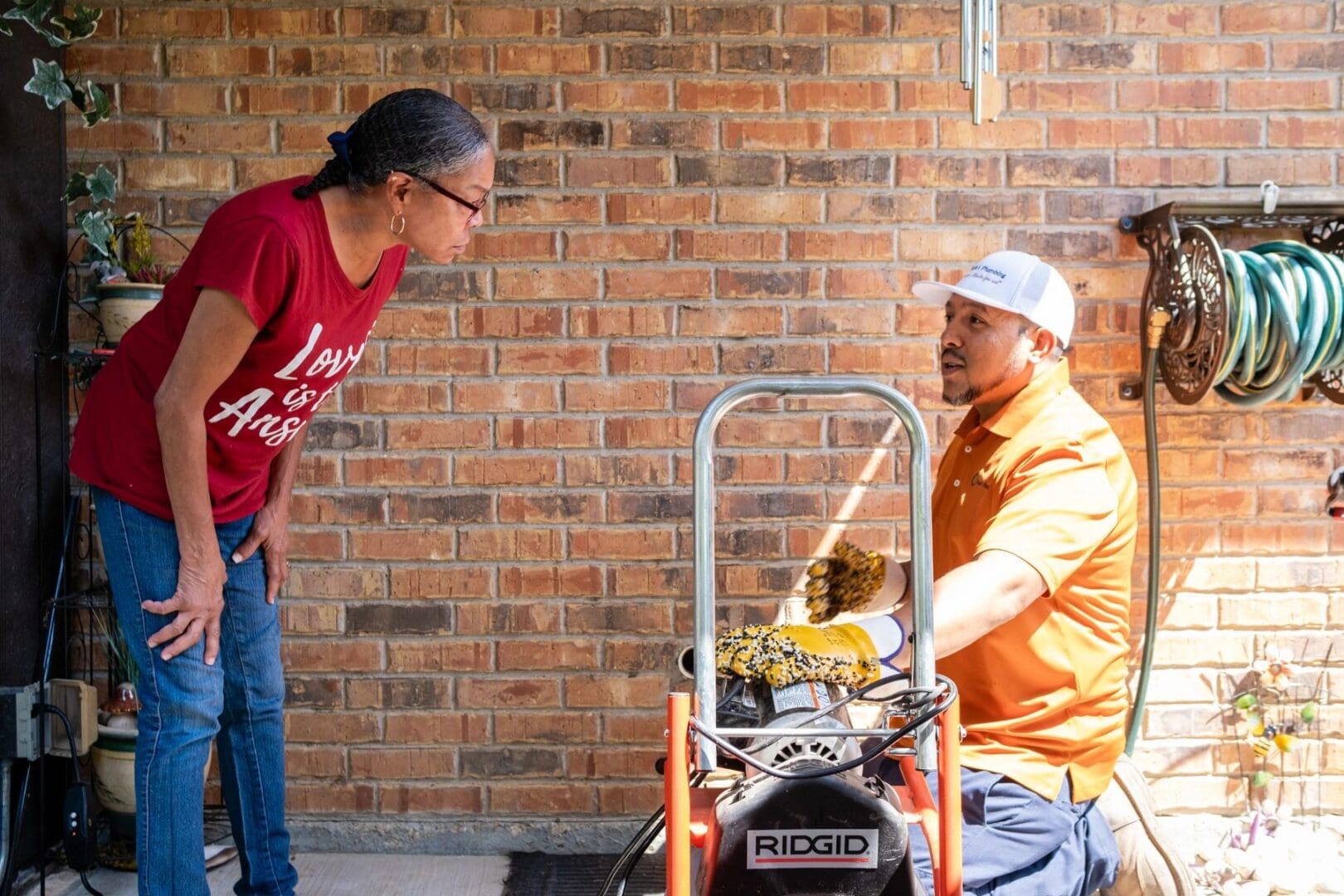 Woman looks at plumber using a drain snake.